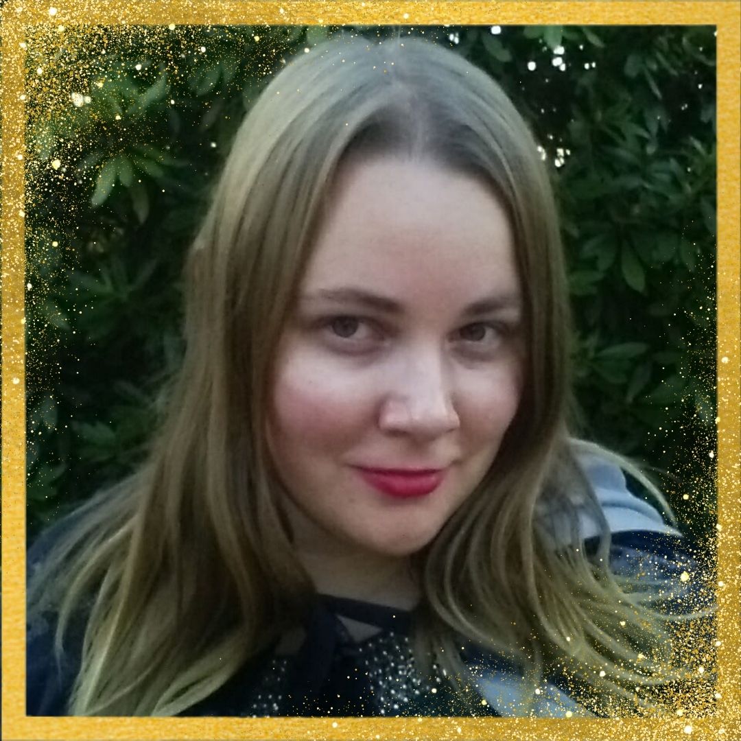 Author Karen Kincy with blonde hair and red lipstick in front of green foliage, framed with a gold border.