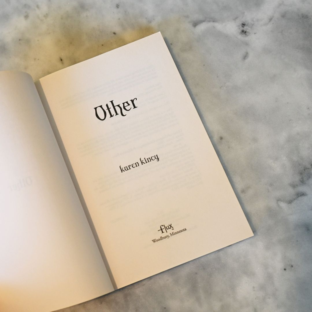 Open book with 'Other' by Karen Kincy on a marble surface
