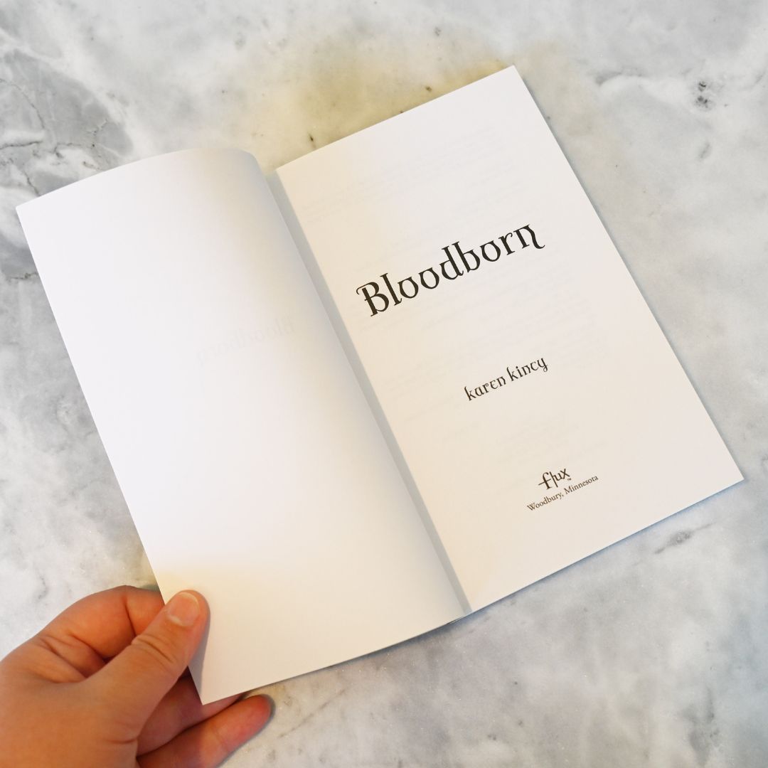 Open book titled 'Bloodborn' held by a hand on a marble surface